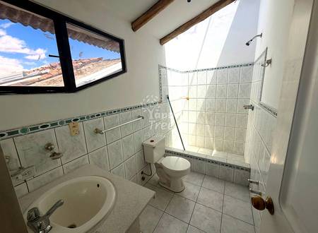 Bathroom with white tile walls, round sink, toilet, shower enclosure, window with mountain view, and wooden ceiling beams.