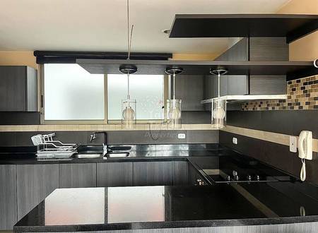 Cocina moderna con gabinetes gris oscuro, encimera de granito negro, fregadero de acero inoxidable y tres lámparas colgantes sobre el mostrador. Backsplash de azulejos visible.