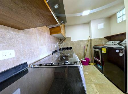 Kitchen with beige tile walls, black countertop, gas stove, sink, overhead cabinets, and black appliances including washing machine and dryer.