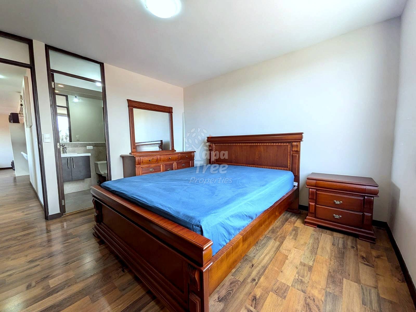 Bedroom with hardwood floors, a wooden bed, blue sheets, a wooden nightstand, and a dresser with mirror.