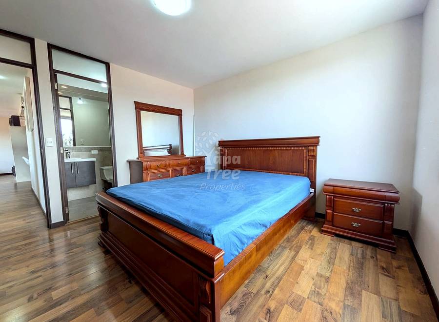 Bedroom with hardwood floors, a wooden bed, blue sheets, a wooden nightstand, and a dresser with mirror.