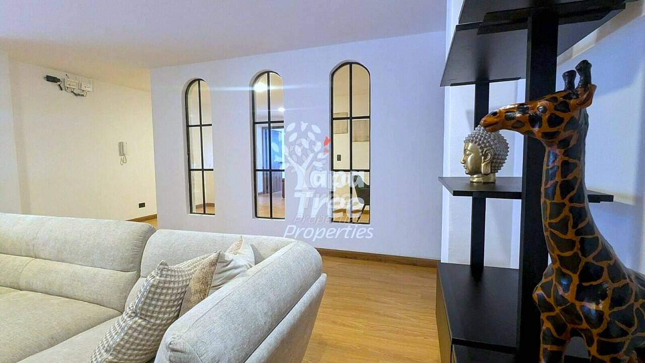 Living room with beige sofa, wooden floor, black metal shelving with giraffe statue, and three arched windows with black frames.