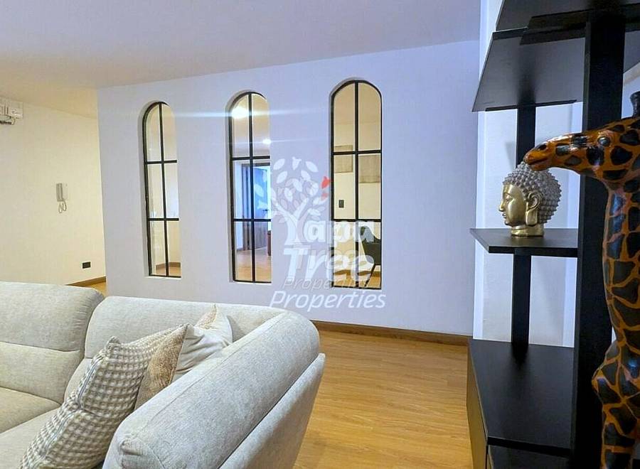 Living room with beige sofa, wooden floor, black metal shelving with giraffe statue, and three arched windows with black frames.