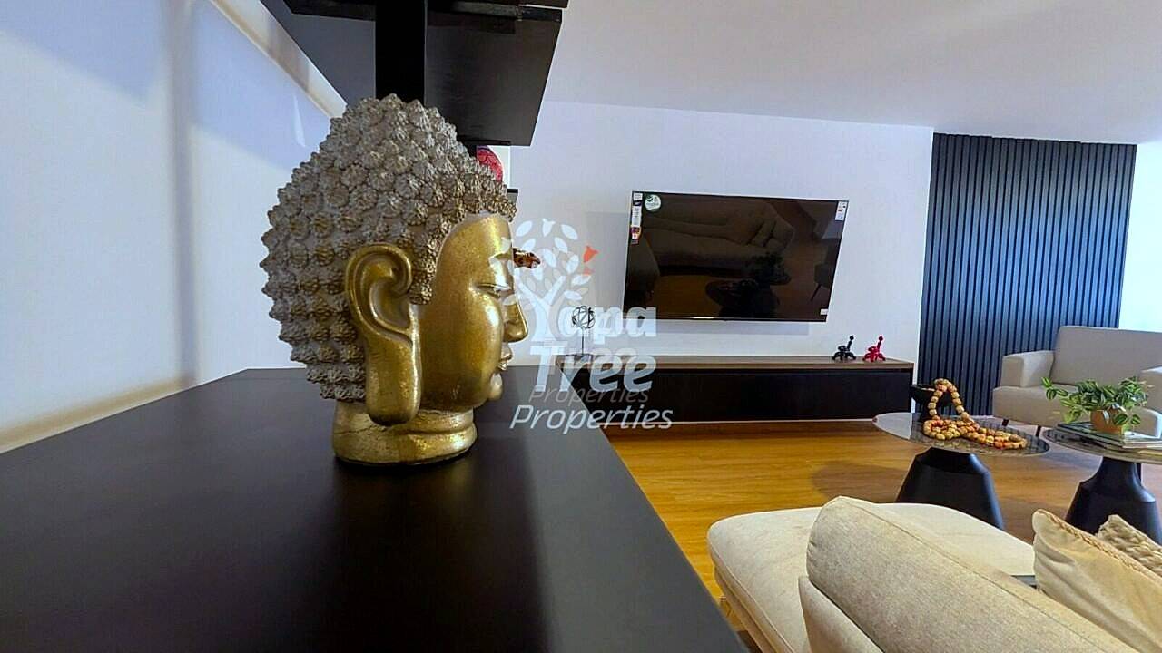 Living room with wooden floor, black dining table, beige sofa, wall-mounted TV, and gold Buddha sculpture decoration.