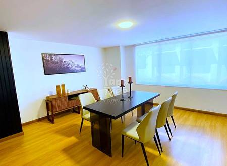 Meeting room with wooden flooring, black dining table, cream chairs, wooden cabinet, framed cityscape photo, recessed ceiling light, and large window with sheer curtains.