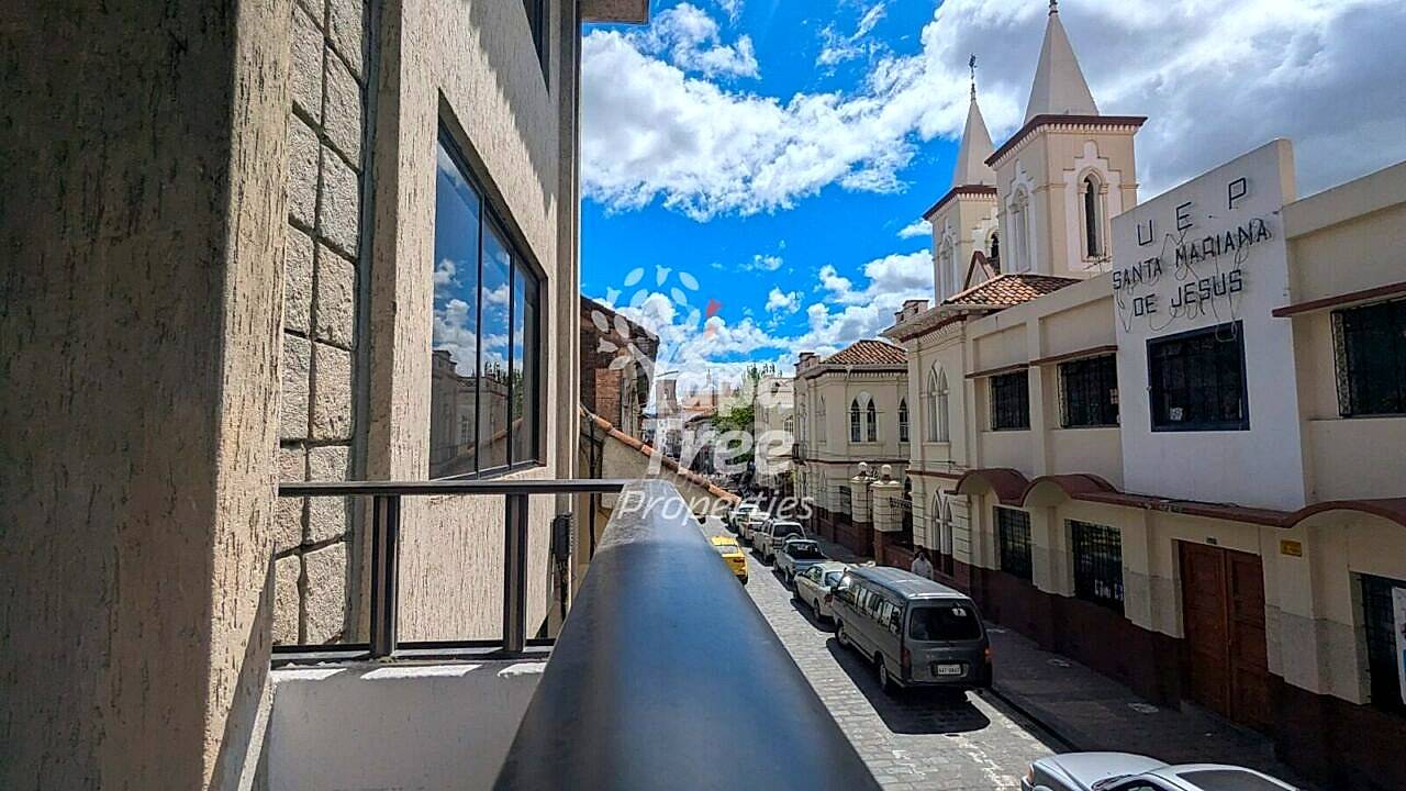Narrow balcony with metal railing overlooking colonial street with church towers and parked vehicles in Cuenca historic center.