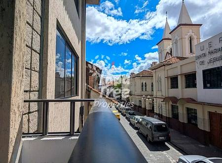Narrow balcony with metal railing overlooking colonial street with church towers and parked vehicles in Cuenca historic center.