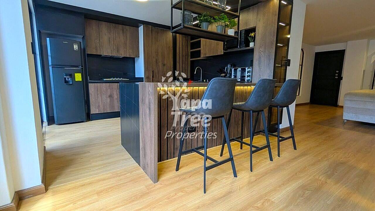 Modern cocina with dark wood cabinetry, black refrigerator, and island counter with three gray bar stools on light wood flooring.