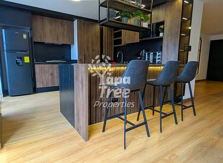 Modern cocina with dark wood cabinetry, black refrigerator, and island counter with three gray bar stools on light wood flooring.
