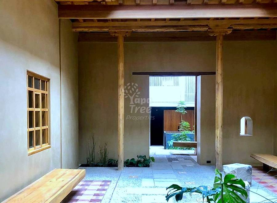 Interior courtyard with exposed wooden beams, tile flooring, wooden bench, potted plants, and doorway opening to garden area.