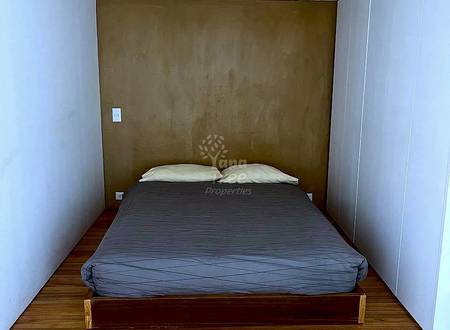 Bedroom with wooden bed, gray bedding, cream pillows, brown accent wall, white side walls, wooden floor, and recessed ceiling lights.