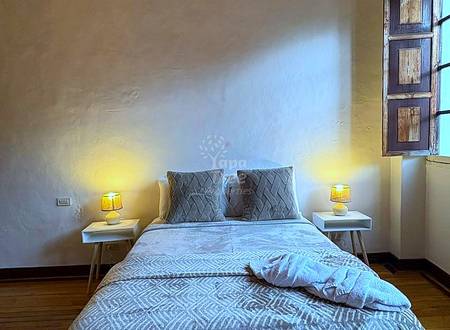 Bedroom with queen bed, patterned bedding, two wooden nightstands with table lamps, decorative wooden ceiling, and window with wooden shutters.