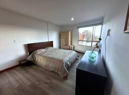 Bedroom with queen bed, dark wood headboard, wooden wardrobe, black desk, recessed lighting, and large window overlooking Cuenca buildings