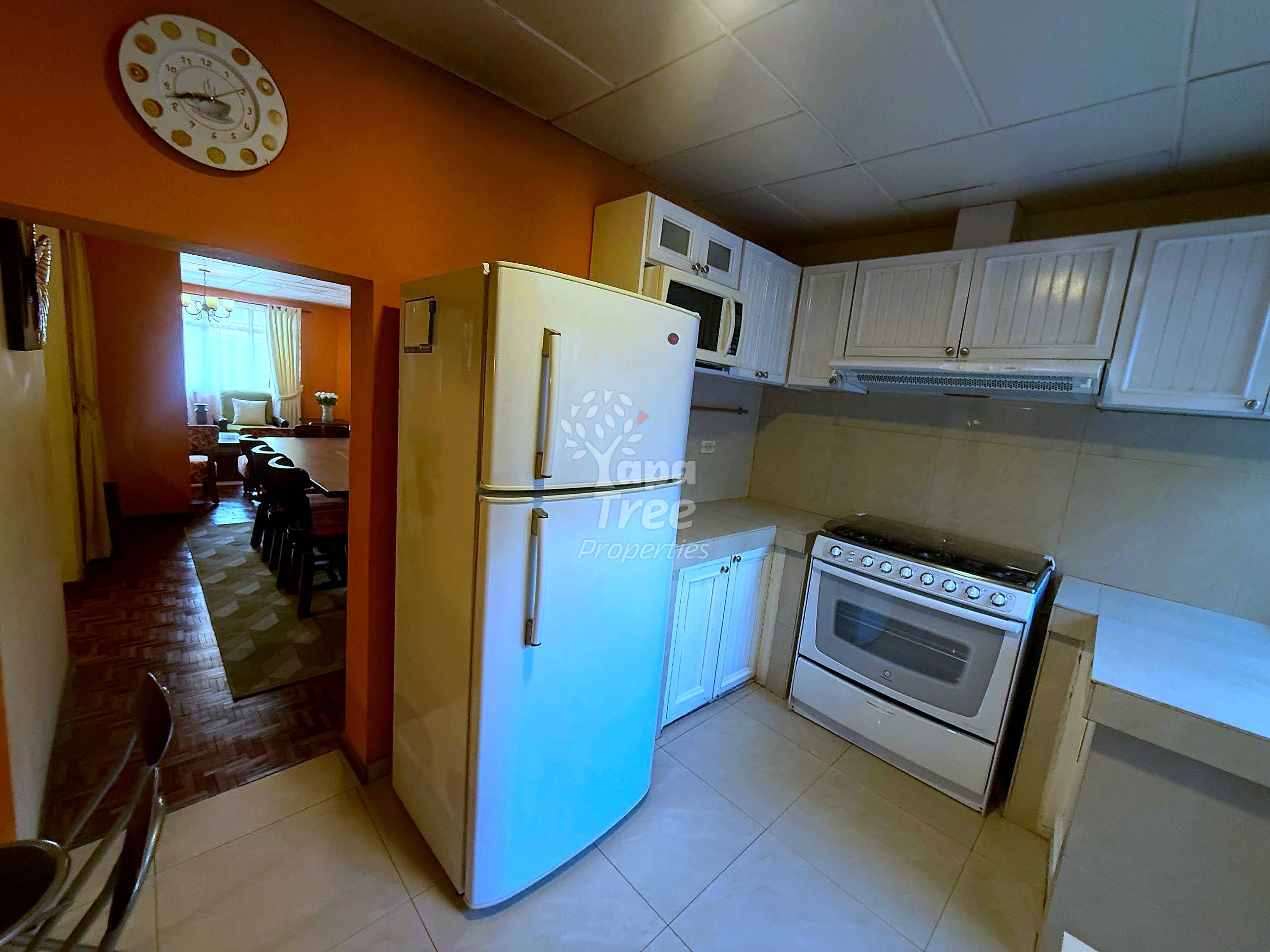Kitchen with cream cabinetry, white refrigerator, gas range, beige tile flooring, orange walls, drop ceiling, and doorway to dining area.