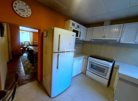 Kitchen with cream cabinetry, white refrigerator, gas range, beige tile flooring, orange walls, drop ceiling, and doorway to dining area.