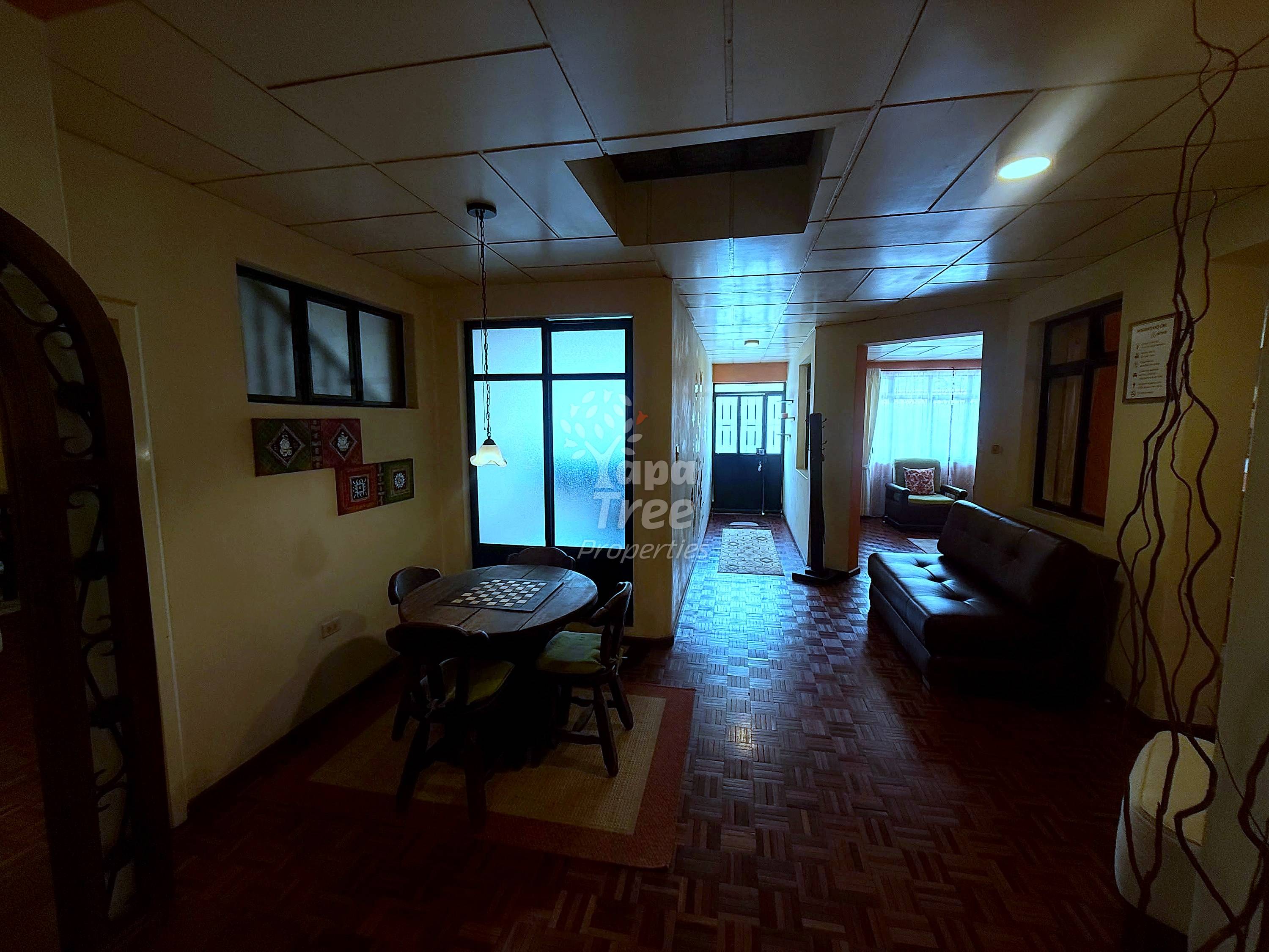 Interior hallway with cream walls, drop ceiling, game table, brown leather sofa, and multiple doorways with natural light.