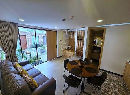 Living and dining area with brown leather sofa, round wooden table with black chairs, tile flooring, glass patio doors, staircase, and recessed ceiling lights.