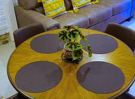Living room with brown leather sofa, yellow patterned pillows, round wood dining table with four brown chairs, and white brick wall.
