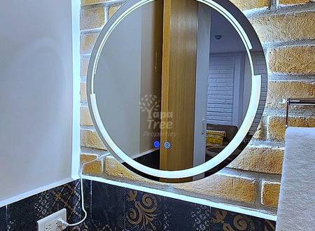Bathroom with round LED-lit mirror, white ceramic sink, black patterned tile backsplash, and exposed brick wall.