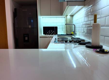 Modern kitchen with white subway tile backsplash, gas cooktop, dark refrigerator, and white countertop with sink and faucet.