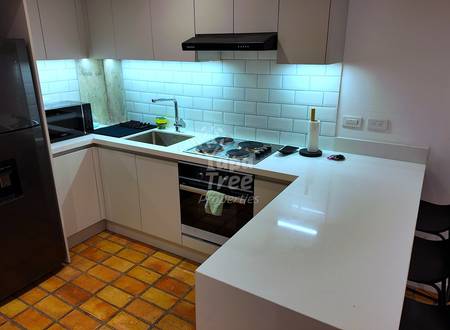 Modern kitchen with white cabinetry, white subway tile backsplash, black refrigerator, built-in black oven, island counter with seating, and terracotta floor tiles.