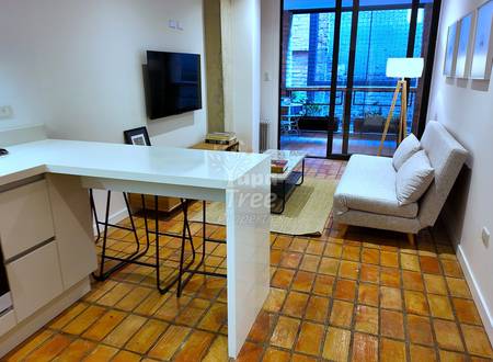 Open-concept suit with white kitchen counter, beige sofa, mounted television, terracotta tile flooring, and glass doors opening to balcony.
