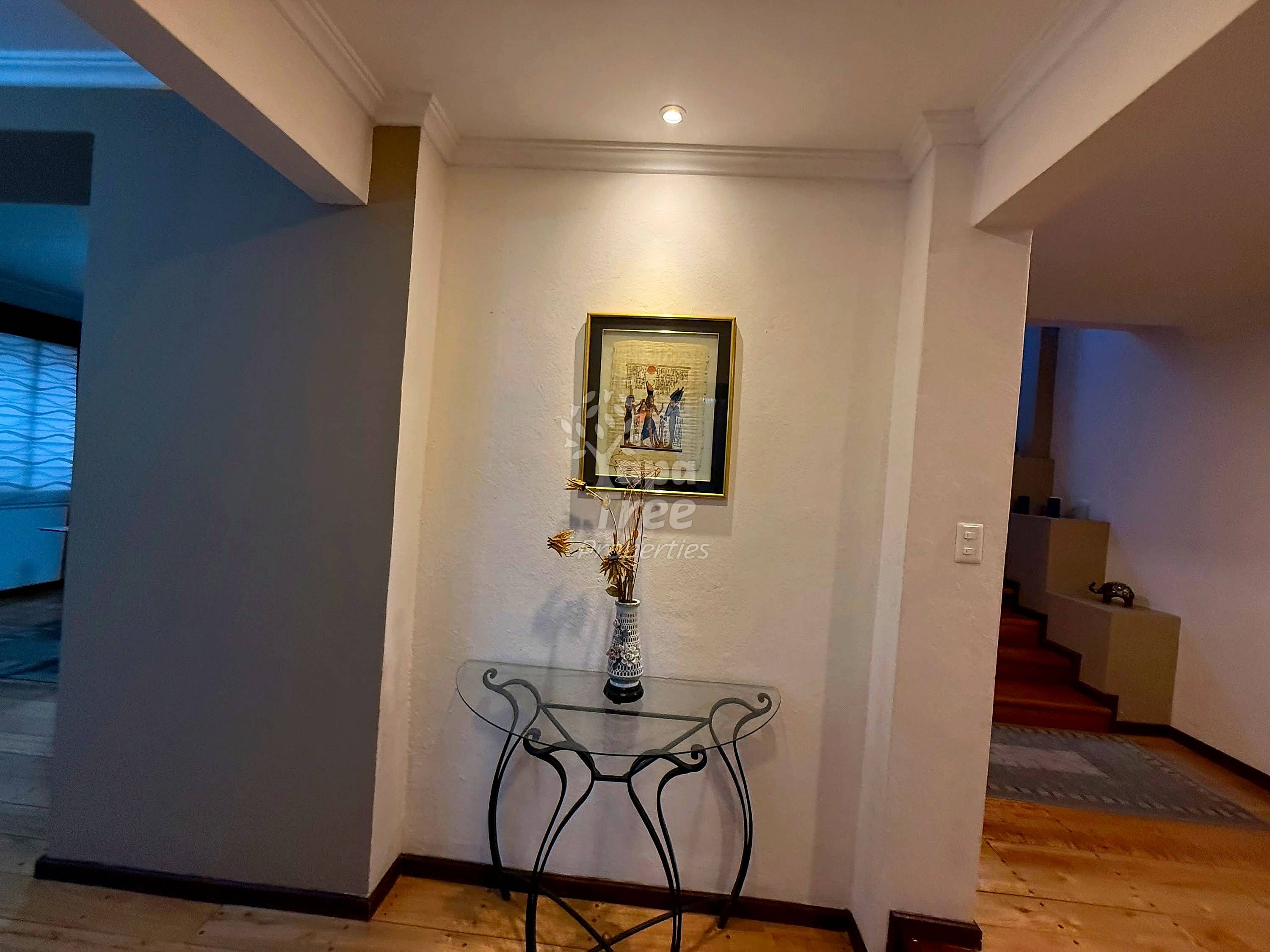 Entryway hallway with white walls, recessed ceiling light, decorative console table with vase, and framed artwork.