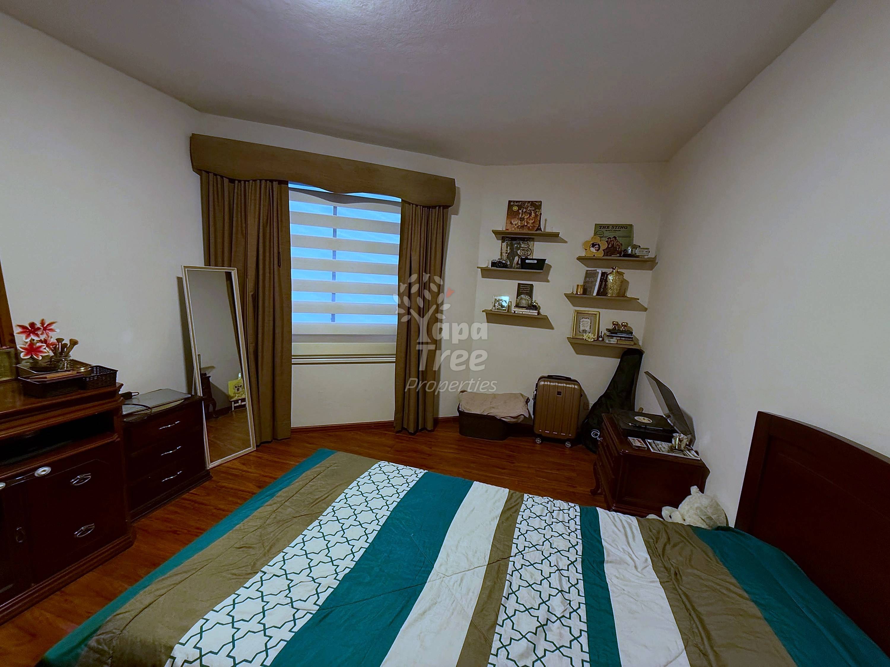 Bedroom with wooden furniture, striped green and cream bedspread, wooden floor, glass door with curtains, wall shelves, and mirror.