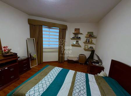Bedroom with wooden furniture, striped green and cream bedspread, wooden floor, glass door with curtains, wall shelves, and mirror.