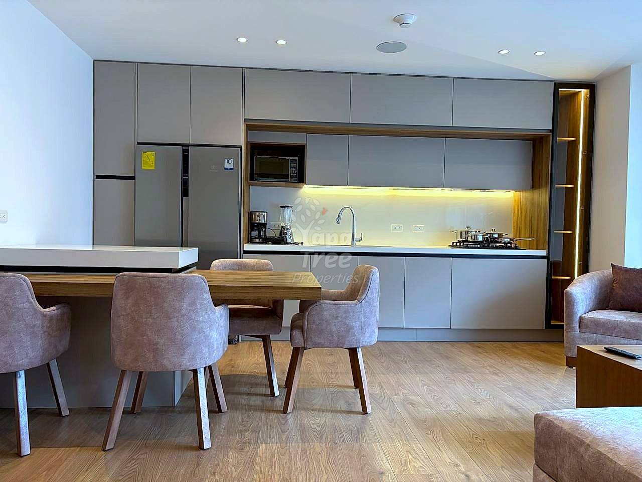 Modern cocina with gray cabinetry, stainless steel appliances, and under-cabinet lighting overlooking dining area with wooden table and upholstered chairs.