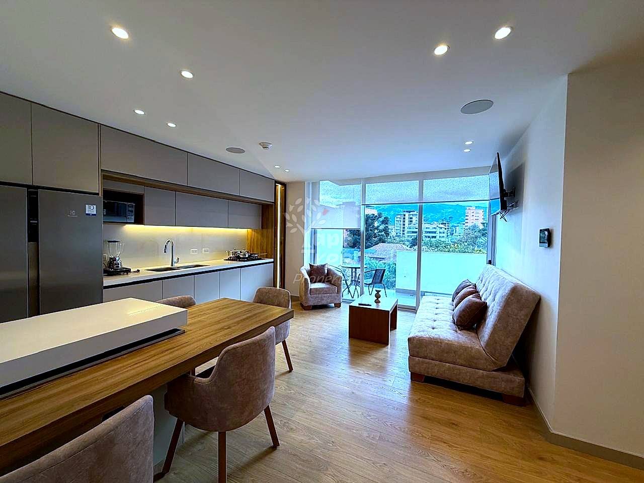 Open-plan departamento with modern kitchen, dining table, brown furniture, wooden flooring, large windows with city views, and recessed ceiling lights.