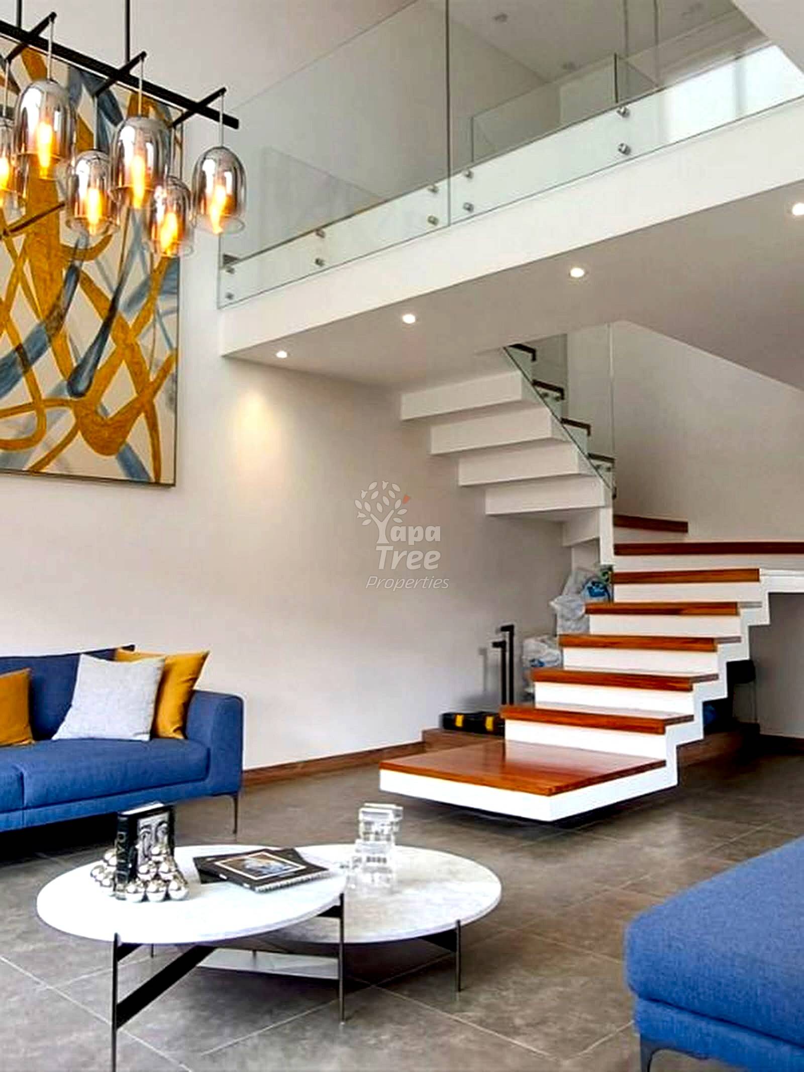 Modern living room with floating staircase, white and wood steps, blue sofa, pendant lighting, and marble coffee table.