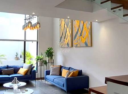 Open-plan living room with blue sofa, white coffee tables, large window, staircase with wood and white design, and framed yellow artwork.