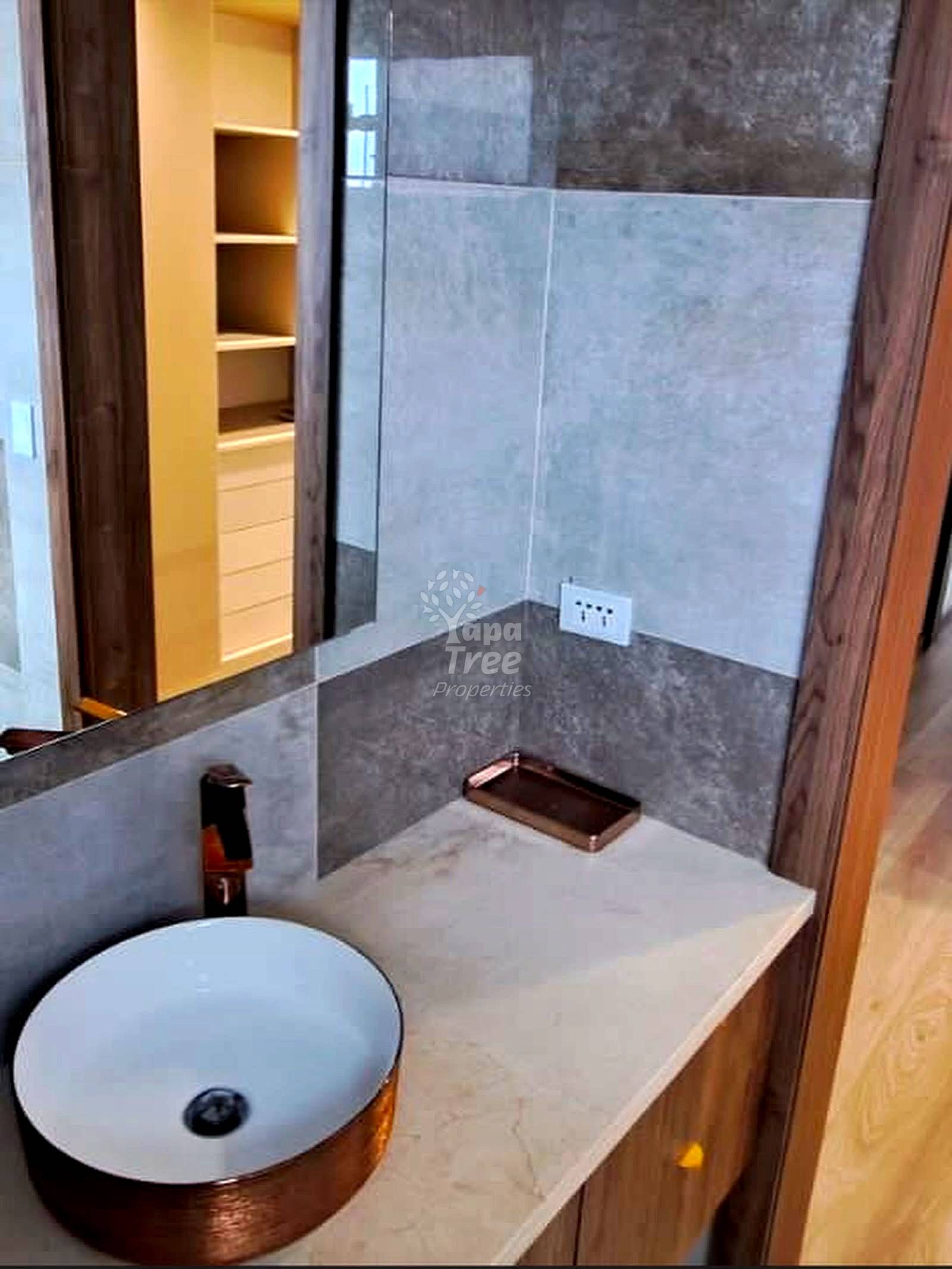 Modern bathroom with round white sink, gray tile walls, glass shower enclosure, and built-in shelving visible through doorway.