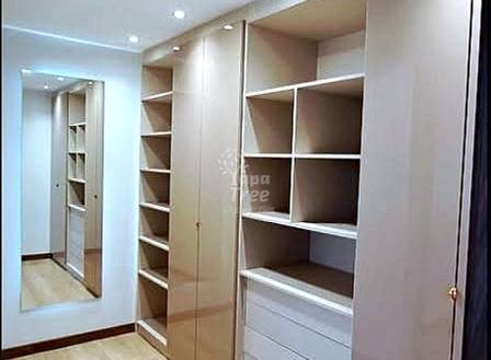 Walk-in closet with built-in wood shelving, mirrored doors, recessed ceiling lights, and light wood flooring.