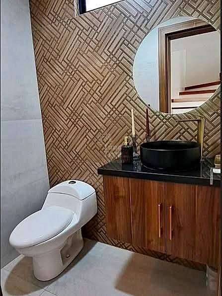 Bathroom with geometric tile walls, wooden vanity cabinet, black countertop, round black sink, and white toilet.