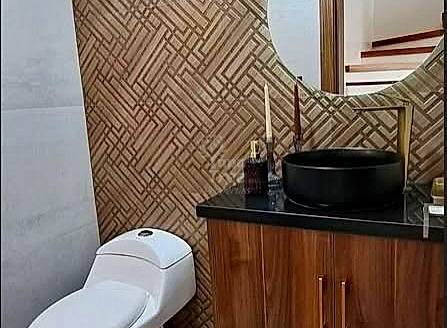 Bathroom with geometric tile walls, wooden vanity cabinet, black countertop, round black sink, and white toilet.