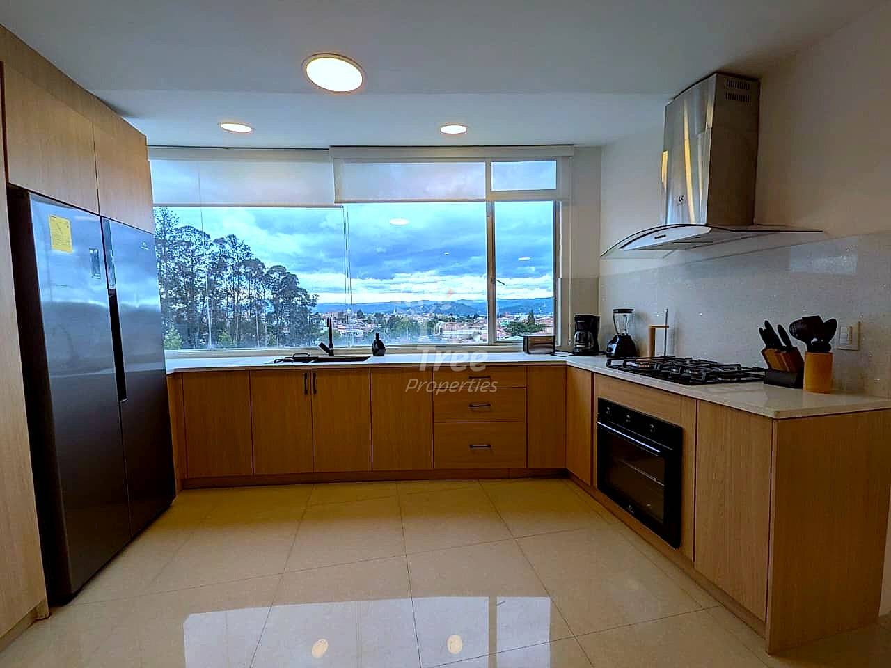 Modern cocina with wood cabinetry, stainless steel appliances, gas cooktop, and large windows overlooking Cuenca valley and mountains.