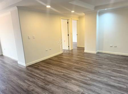 Sala vacía con paredes color crema, piso de madera laminada, luces empotradas en techo, y dos puertas blancas interiores.