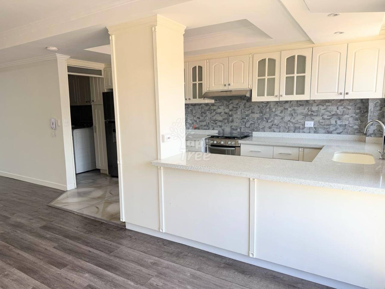 Open-concept kitchen with white cabinetry, granite countertop island, gray tile backsplash, stainless steel stove, and wood-look flooring extending to adjacent living area