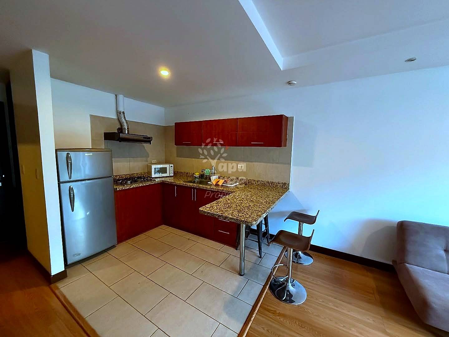 Modern cocina with dark red cabinets, granite countertop, stainless steel appliances, and breakfast bar with two stools, connected to living area.