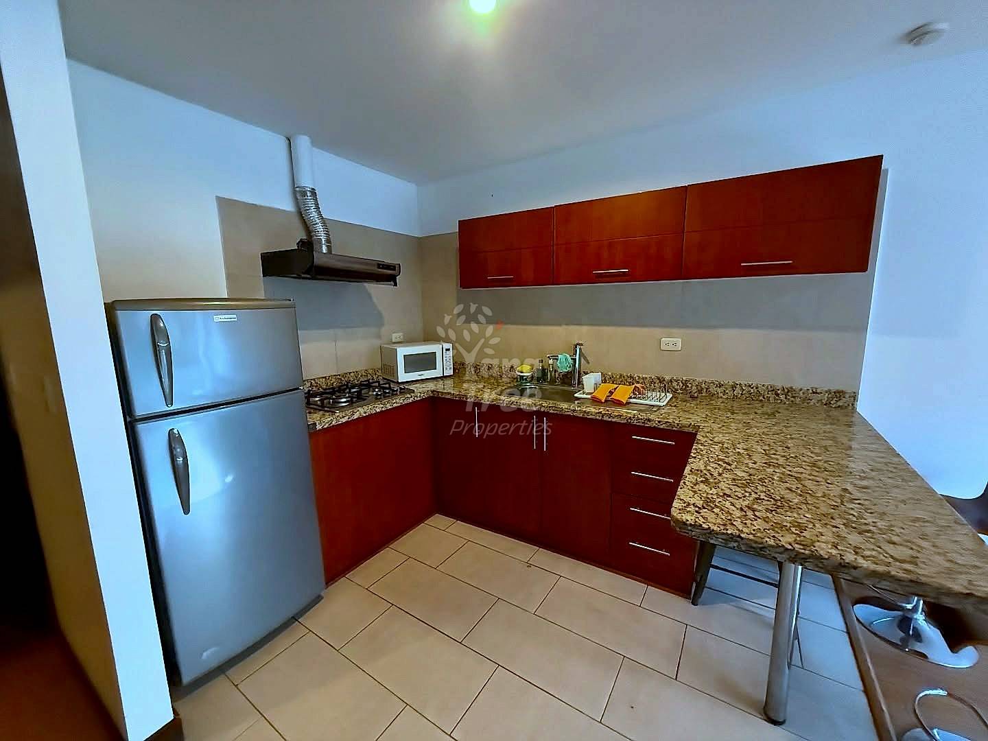 Cocina with dark wood cabinetry, granite countertops, stainless steel refrigerator, gas stovetop, microwave, and tile flooring.