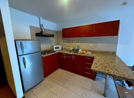 Cocina with dark wood cabinetry, granite countertops, stainless steel refrigerator, gas stovetop, microwave, and tile flooring.