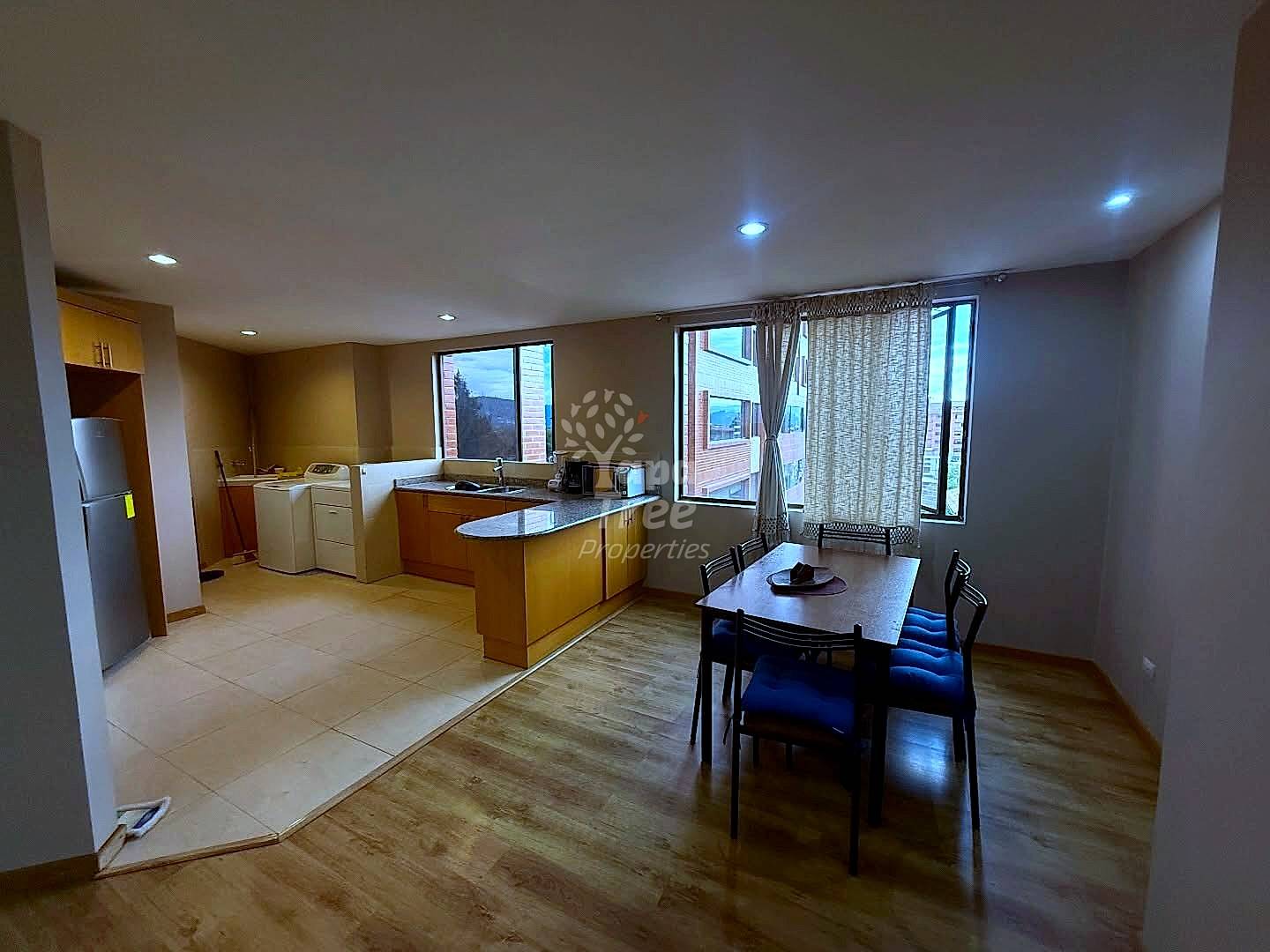 Open concept dining and kitchen area with wooden cabinetry, tile countertops, dining table with blue chairs, and mountain views through large windows.