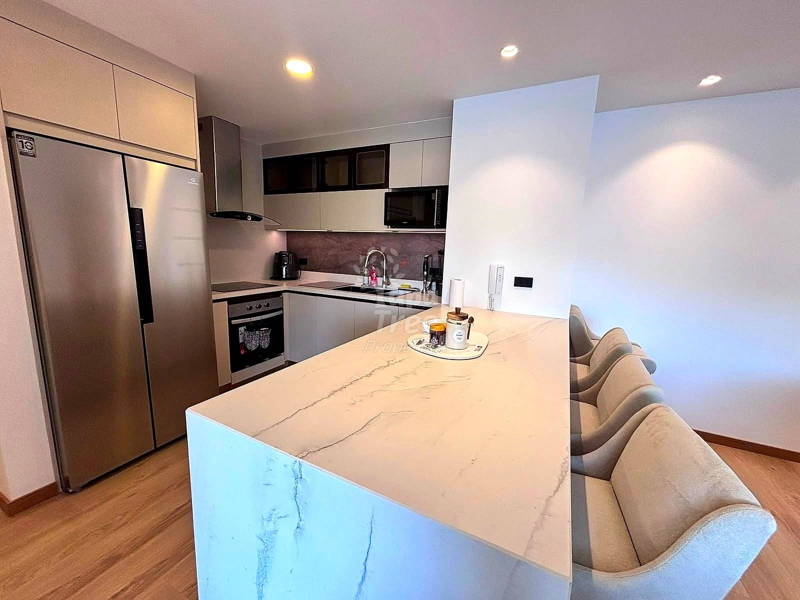 Modern kitchen with white and black cabinetry, stainless steel refrigerator, island with marble countertop, and beige upholstered bar seating.