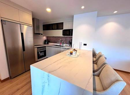 Modern kitchen with white and black cabinetry, stainless steel refrigerator, island with marble countertop, and beige upholstered bar seating.
