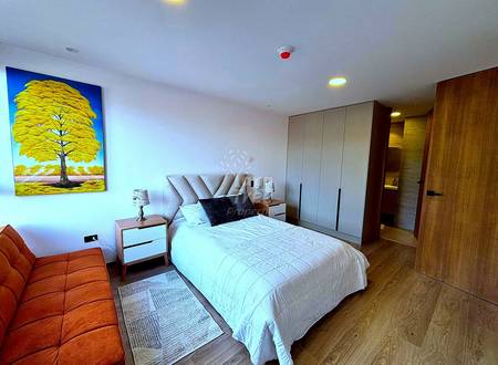 Master bedroom with queen bed, gray upholstered headboard, wood nightstands, cream wardrobe cabinets, orange sofa, wood flooring, and recessed ceiling lights.