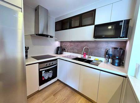 Modern kitchen with white cabinetry, black and stainless steel appliances, gray tile backsplash, and wood-grain flooring.