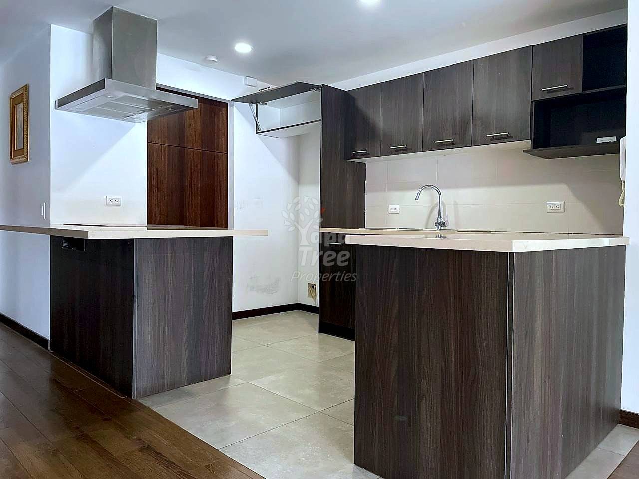 Modern cocina with dark wood cabinetry, stainless steel range hood, white countertops, tile flooring, and recessed ceiling lights.