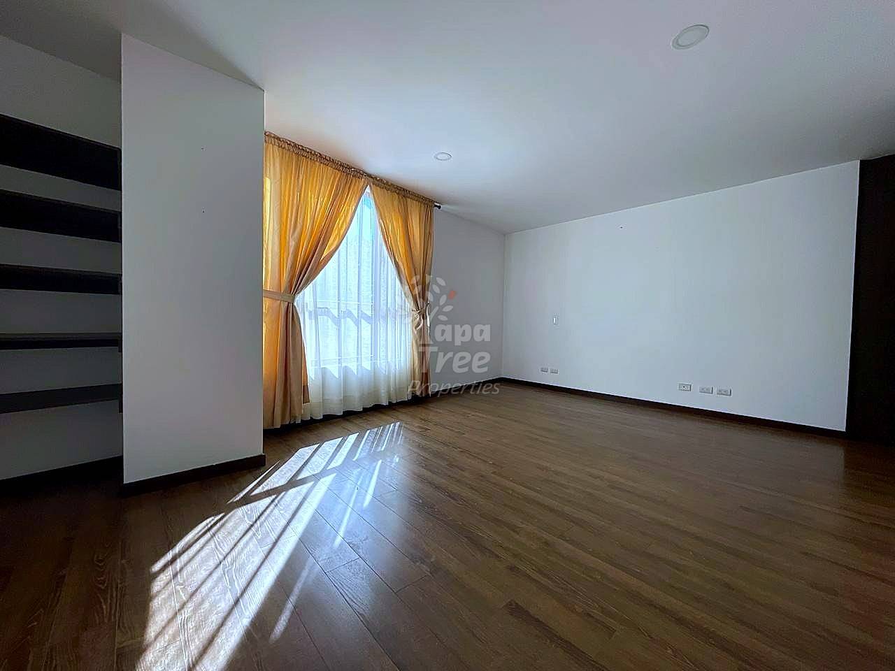 Empty bedroom with wood flooring, white walls, gold curtains on window, built-in shelving, and recessed lighting.